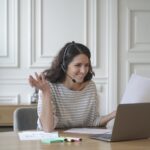 Young excited cheerful female coach in headset with microphone conducts private consultations online