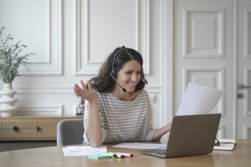 Young excited cheerful female coach in headset with microphone conducts private consultations online