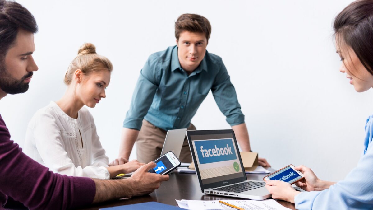 Young businesspeople using digital devices with facebook logo icons on screens