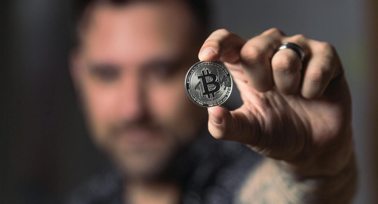 Adult male hand holding a Bitcoin, showcasing cryptocurrency focus indoors.
