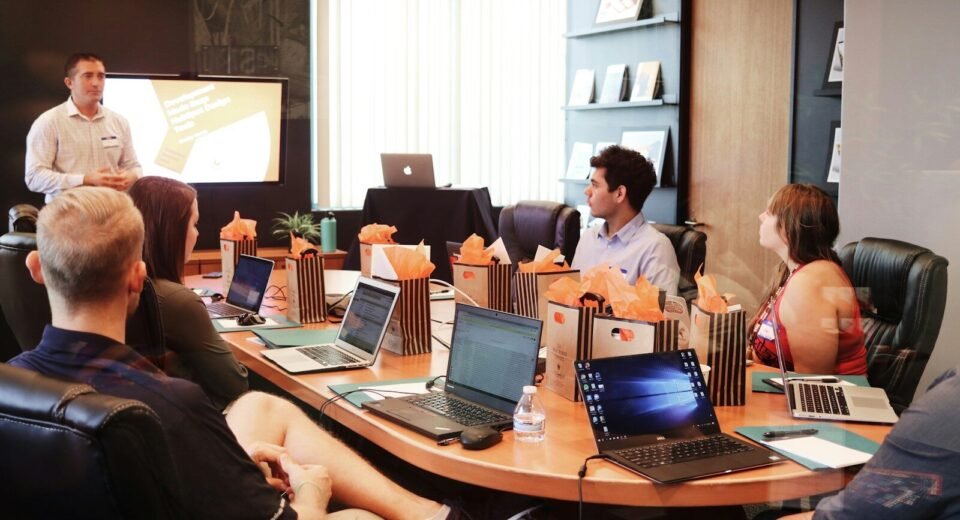 Coaching Business man standing in front of people sitting beside table with laptop computers